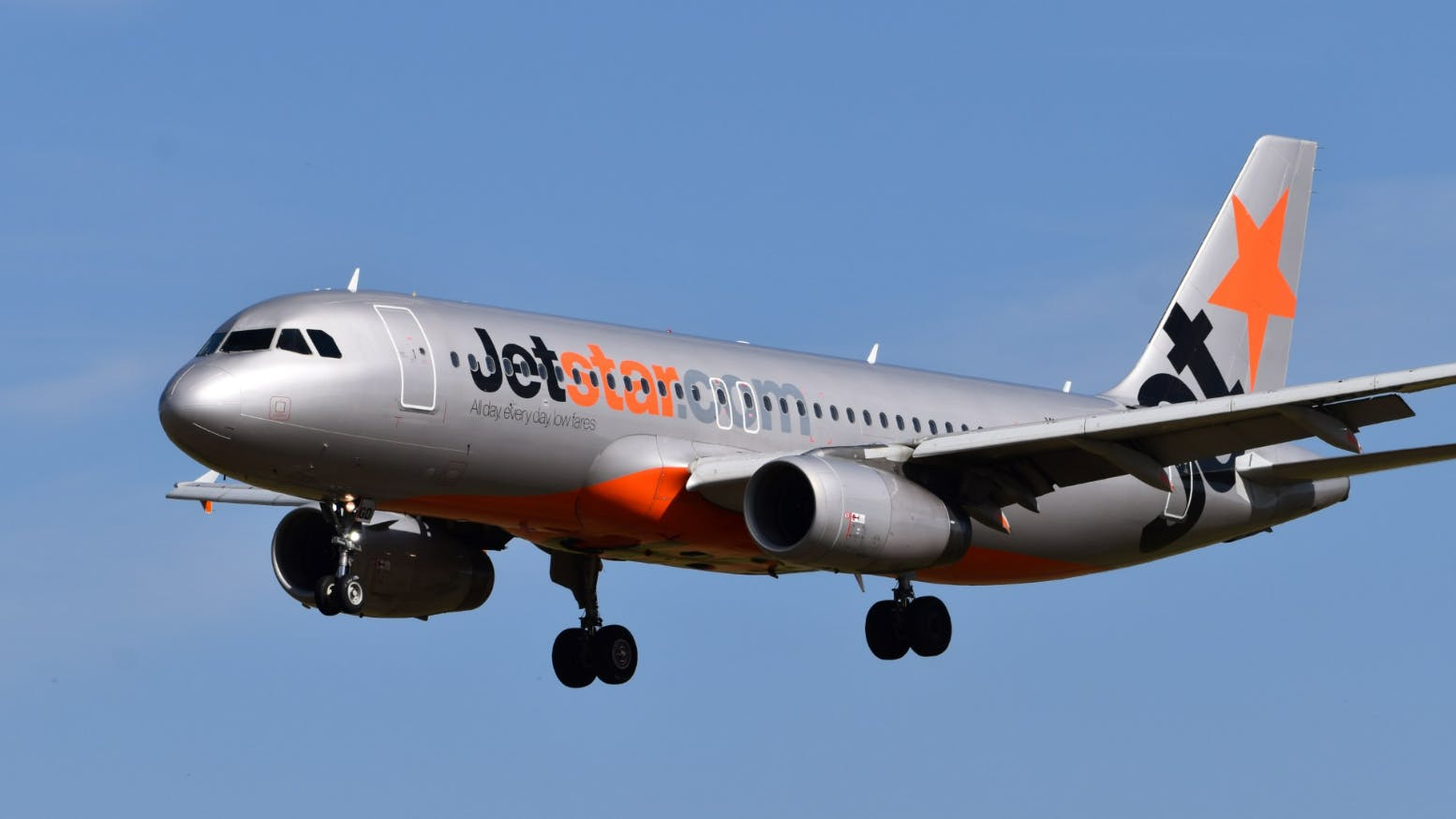 A gray airplane flying in a blue sky with blue and orange text on the side that reads: Jet Star