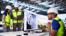 A man wearing a high-visibility vest and hard hat looking at aircraft maintenance data on a desktop computer, with two other maintenance technicians looking at a tablet in the background A man wearing a high-visibility vest and hard hat looking at aircraft maintenance data on a desktop computer, with two other maintenance technicians looking at a tablet in the background