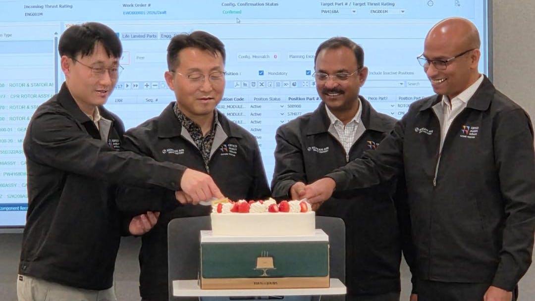 Four men cutting a celebratory cake while standing in front of a projection of an Excel sheet