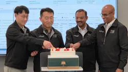 Four men cutting a celebratory cake while standing in front of a projection of an Excel sheet Four men cutting a celebratory cake while standing in front of a projection of an Excel sheet