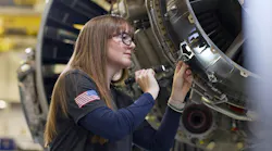 A woman shining a flashlight on an airplane engine and inspecting it carefully