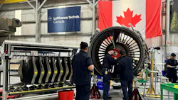 Three aviation maintenance technicians working on a large, black airplane engine, with a Canadian flag and a banner that reads 'Lufthansa Technik Canada' behind the engine Three aviation maintenance technicians working on a large, black airplane engine, with a Canadian flag and a banner that reads 'Lufthansa Technik Canada' behind the engine