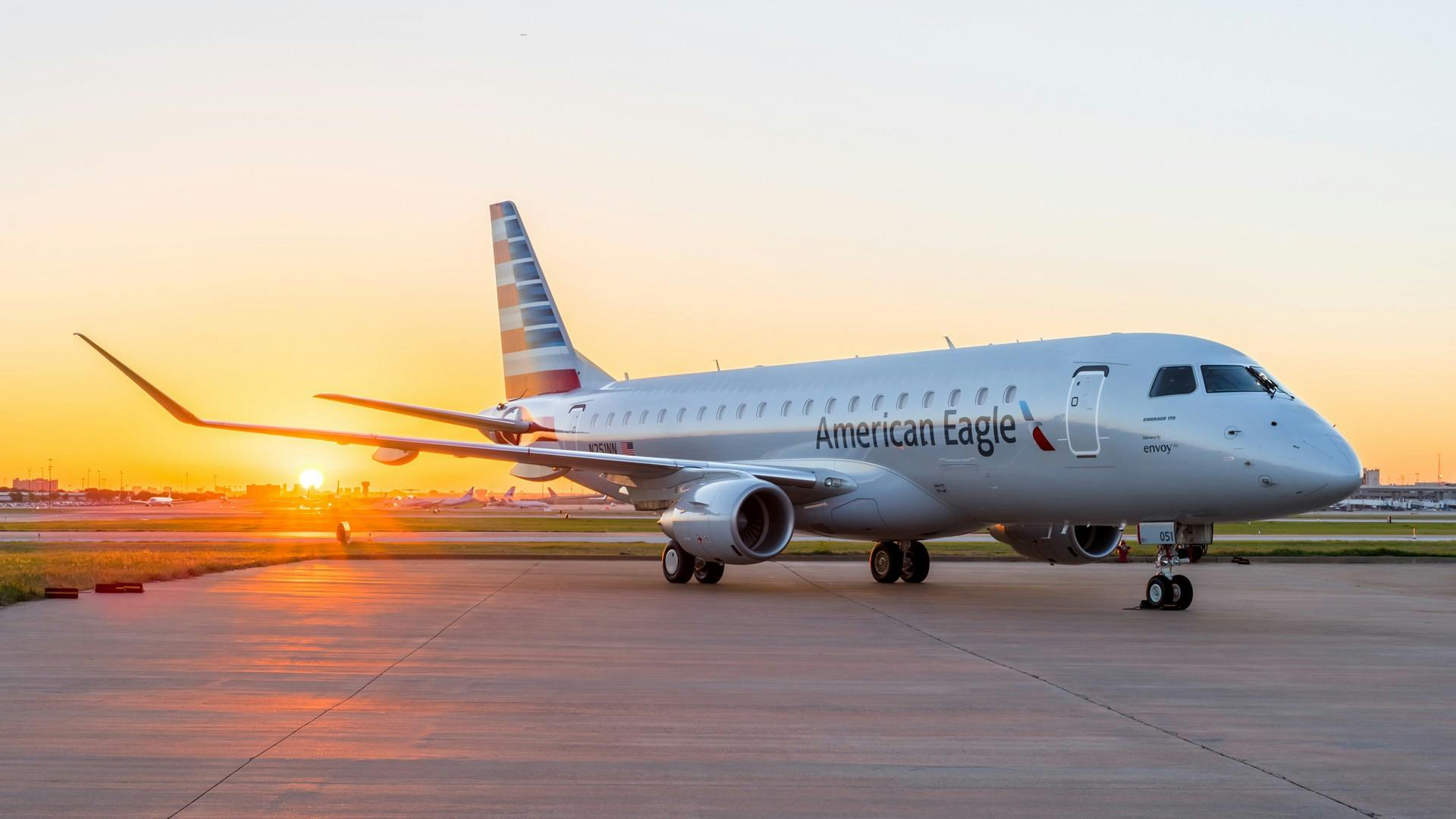 A large airplane with 'American Eagle' printed on the side parked on a tarmac with a sunset behind it