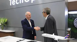 Two men wearing suits shaking hands while standing behind a desk displaying a model airplane Two men wearing suits shaking hands while standing behind a desk displaying a model airplane