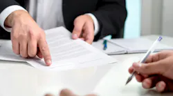 A close-up shot of a table with a person wearing a suit holding a paper and pointing and another person writing A close-up shot of a table with a person wearing a suit holding a paper and pointing and another person writing