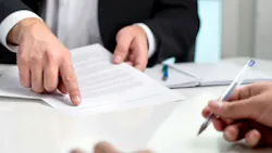 A close-up shot of a table with a person wearing a suit holding a paper and pointing and another person writing A close-up shot of a table with a person wearing a suit holding a paper and pointing and another person writing