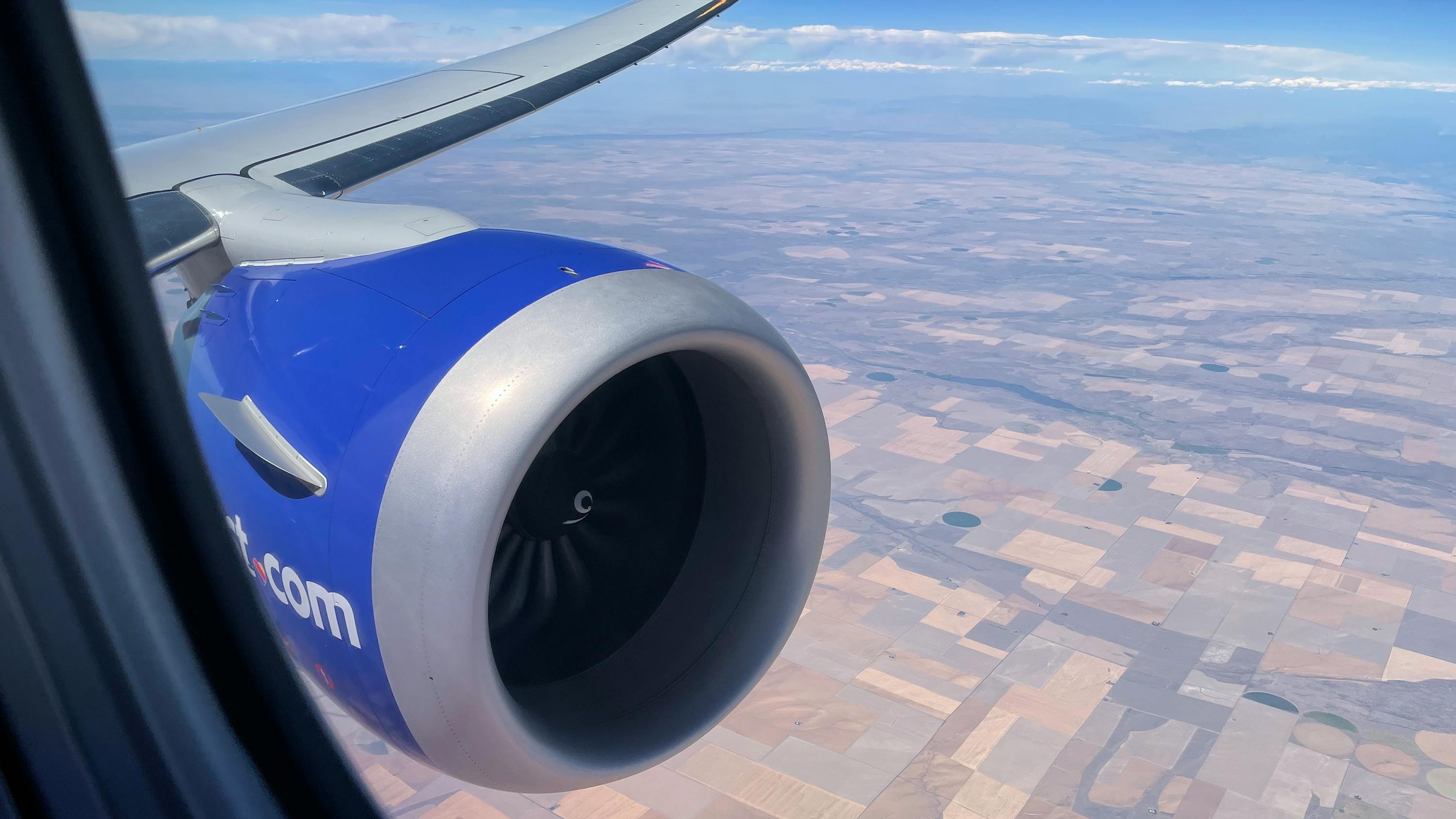 A zoomed-in perspective of a blue airplane engine attached to a plane flying over plots of land