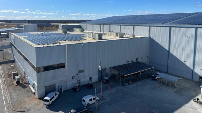 An aerial photograph of two large warehouse-like buildings with solar panels installed on both roofs