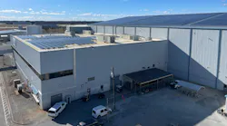 An aerial photograph of two large warehouse-like buildings with solar panels installed on both roofs