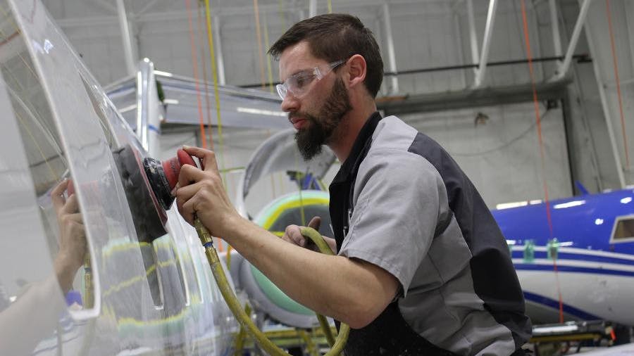 A man wearing PPE using a handheld machine to work on the coatings on the surface of an airplane