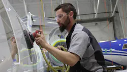 A man wearing PPE using a handheld machine to work on the coatings on the surface of an airplane A man wearing PPE using a handheld machine to work on the coatings on the surface of an airplane