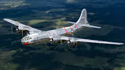 A silver military airplane with red accents flying over lush green land A silver military airplane with red accents flying over lush green land