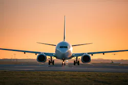 An airplane landing on a runway with an orange sunset behind it An airplane landing on a runway with an orange sunset behind it