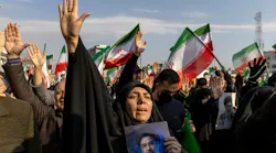 A woman holding a photograph of a man and raising her hand in the air in front of a large crowd of people raising their hands and Iranian flags A woman holding a photograph of a man and raising her hand in the air in front of a large crowd of people raising their hands and Iranian flags
