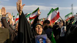 A woman holding a photograph of a man and raising her hand in the air in front of a large crowd of people raising their hands and Iranian flags A woman holding a photograph of a man and raising her hand in the air in front of a large crowd of people raising their hands and Iranian flags