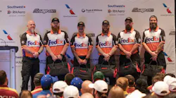Six men wearing FedEx shirts standing in a line on a stage and smiling at the camera Six men wearing FedEx shirts standing in a line on a stage and smiling at the camera