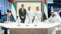 Two men sit at a table with flags on it, signing documents, while three men stand behind the table Two men sit at a table with flags on it, signing documents, while three men stand behind the table
