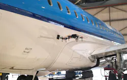 A black drone hovering next to a white and blue airplane inside a hangar A black drone hovering next to a white and blue airplane inside a hangar