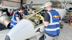 Three aviation maintenance technicians wearing blue vests working on an opened-up airplane inside a hangar Three aviation maintenance technicians wearing blue vests working on an opened-up airplane inside a hangar