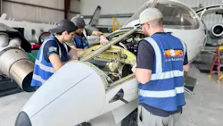 Three aviation maintenance technicians wearing blue vests working on an opened-up airplane inside a hangar Three aviation maintenance technicians wearing blue vests working on an opened-up airplane inside a hangar