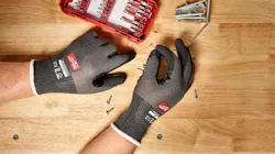 A pair of hands wearing black gloves and holding a screw over a wooden table A pair of hands wearing black gloves and holding a screw over a wooden table