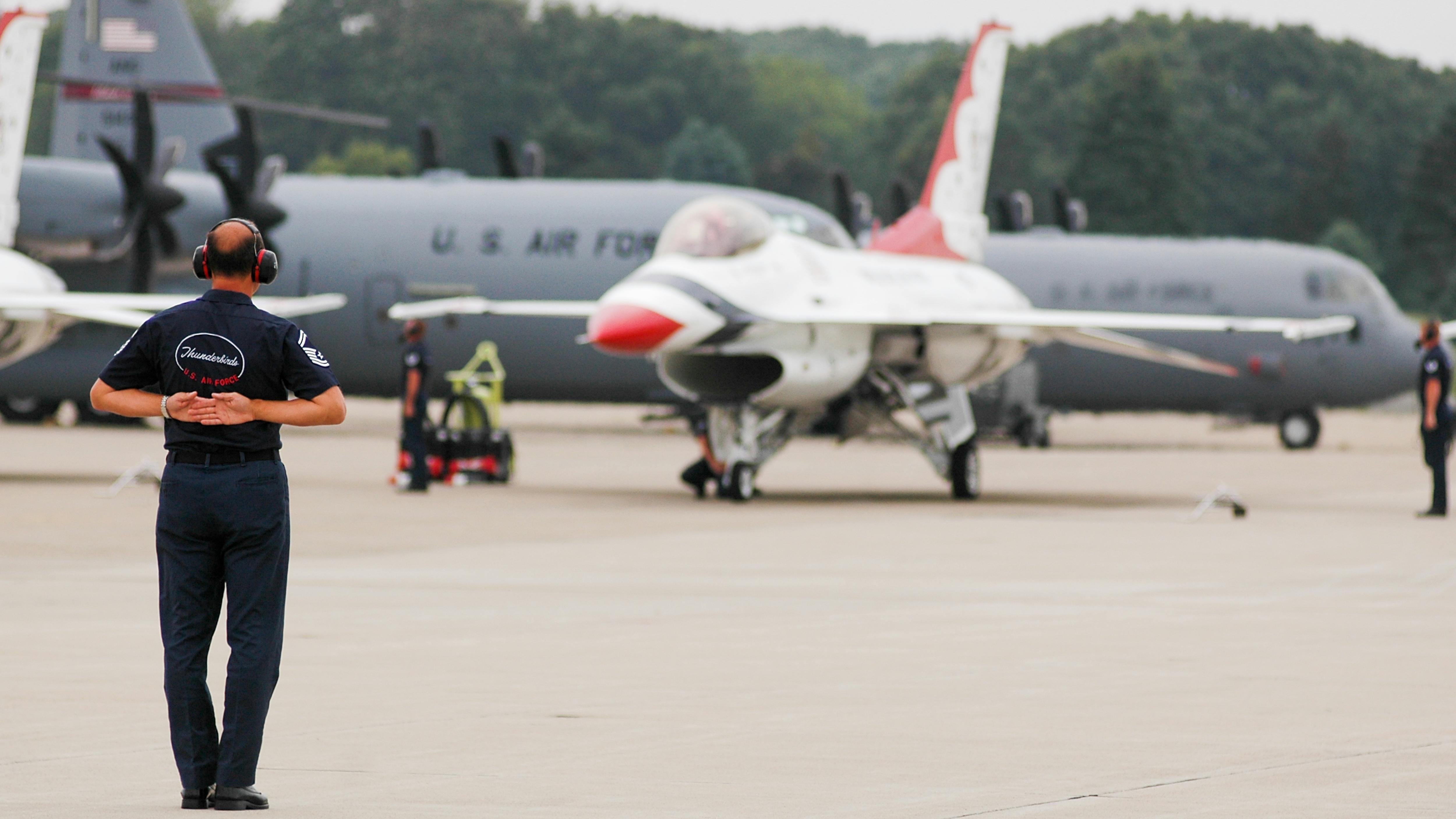 A man standing on a runway looking at an airplane parked on the ground, with aircraft in the background labeled 'U.S. Air Force'