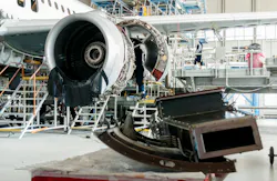 An aircraft component on a work table with an opened-up airplane engine behind it on a stand An aircraft component on a work table with an opened-up airplane engine behind it on a stand