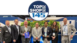 A line of people wearing business attire and ID badges smiling at the camera, with one man holding an award plaque, with a graphic at the top of the image that reads: TOP SHOP 2026 the 145 A line of people wearing business attire and ID badges smiling at the camera, with one man holding an award plaque, with a graphic at the top of the image that reads: TOP SHOP 2026 the 145