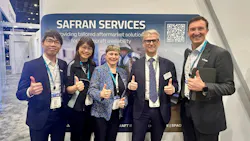 A group of men and women wearing business attire and ID badges, smiling and giving a thumbs-up to the camera while standing in front of a sign that reads, 'Safran Services' A group of men and women wearing business attire and ID badges, smiling and giving a thumbs-up to the camera while standing in front of a sign that reads, 'Safran Services'