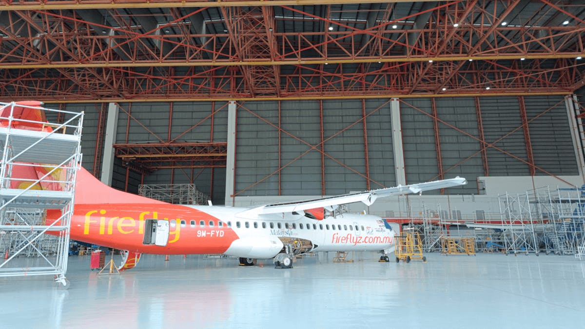 A white and red airplane with 'Firefly' printed on the side parked inside a maintenance hangar with the facility door open