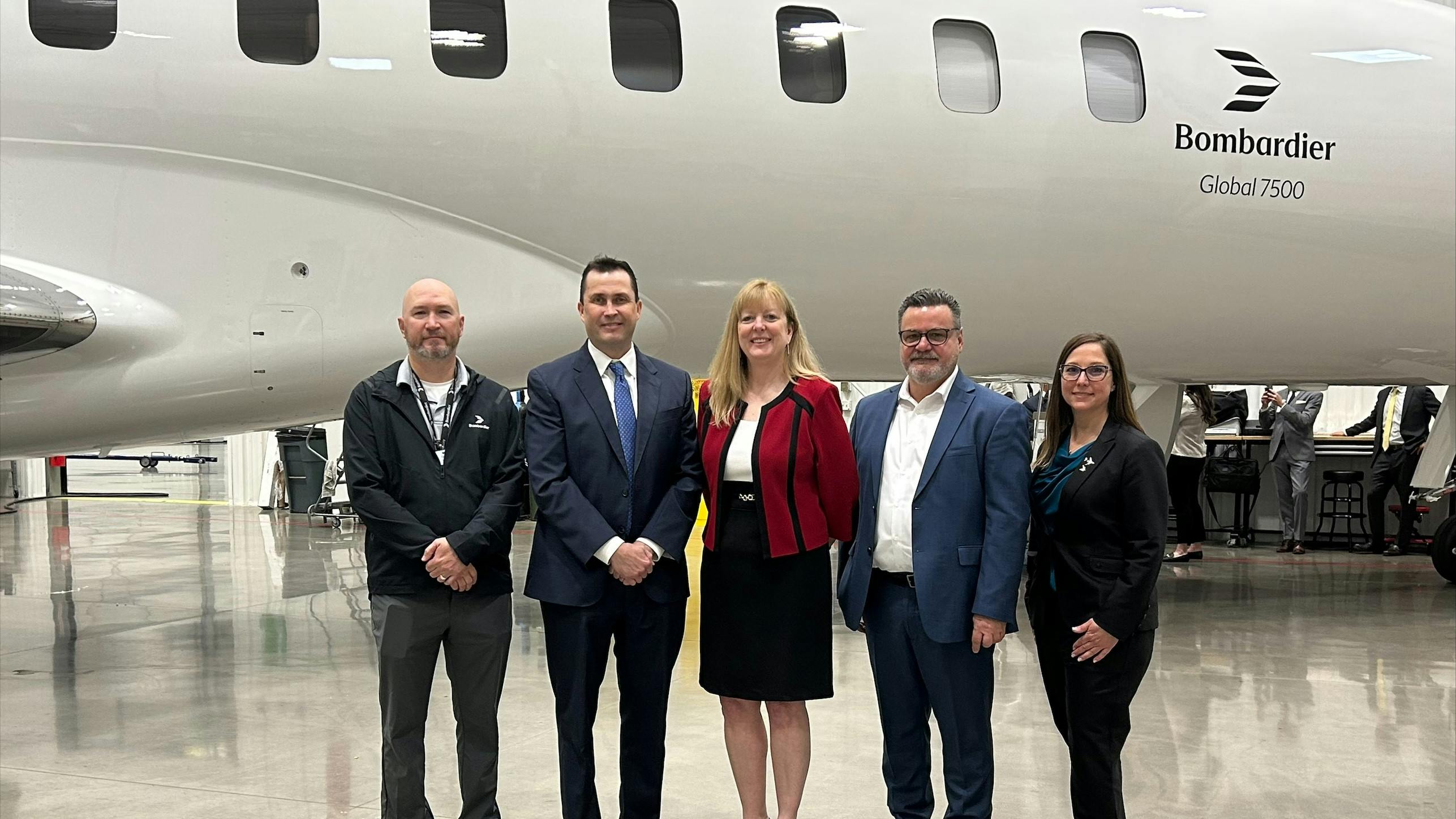 A group of professionals wearing business attire smiling at the camera and standing in front of a white airplane with 'Bombardier Global 7500' printed on the side
