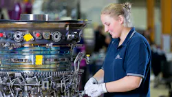 A woman wearing a blue shirt and white gloves working on an aircraft component that's removed from the airplane A woman wearing a blue shirt and white gloves working on an aircraft component that's removed from the airplane