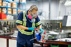 A man wearing a dark blue shirt and PPE equipment using pliers on an aircraft component A man wearing a dark blue shirt and PPE equipment using pliers on an aircraft component