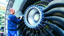 A man wearing a blue uniform placing a turbine blade in an airplane engine A man wearing a blue uniform placing a turbine blade in an airplane engine
