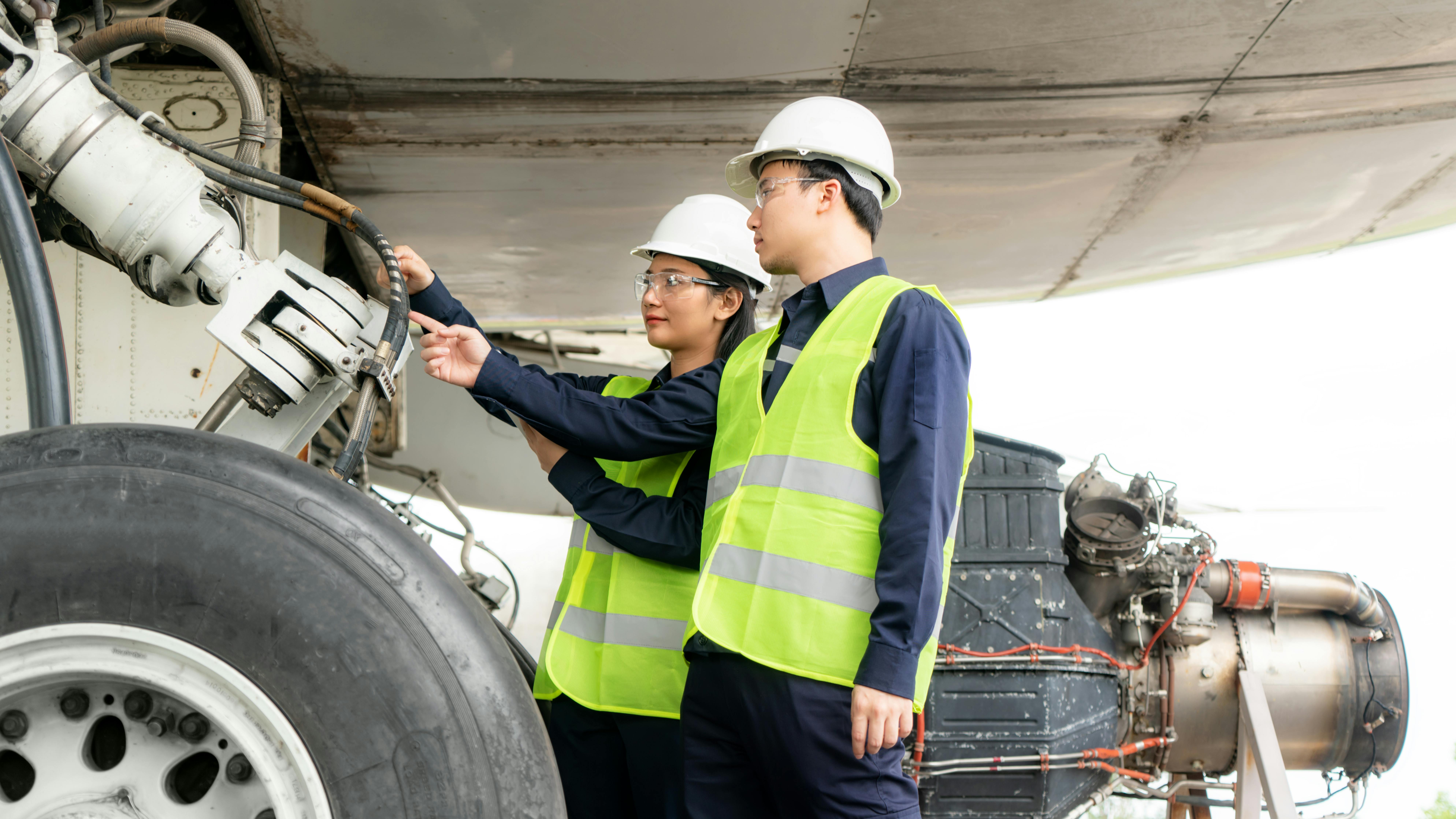 Two maintenance technicians wearing high-visibility vests inspecting an airplane's landing gear