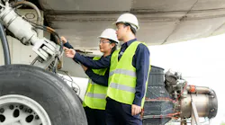 Two maintenance technicians wearing high-visibility vests inspecting an airplane's landing gear