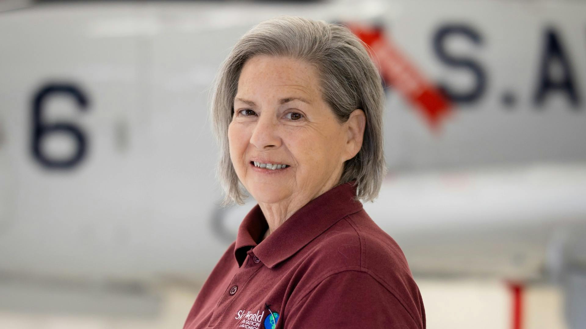 A close-up shot of a woman wearing a maroon polo shirt smiling at the camera
