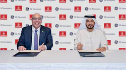Two men sitting at a table and smiling at the camera while signing documents in front of a backdrop displaying the logos for GE Aerospace and Emirates