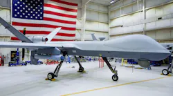 A large white aircraft with no windows parked in a hangar with an American flag hanging in the background