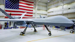 A large white aircraft with no windows parked in a hangar with an American flag hanging in the background A large white aircraft with no windows parked in a hangar with an American flag hanging in the background