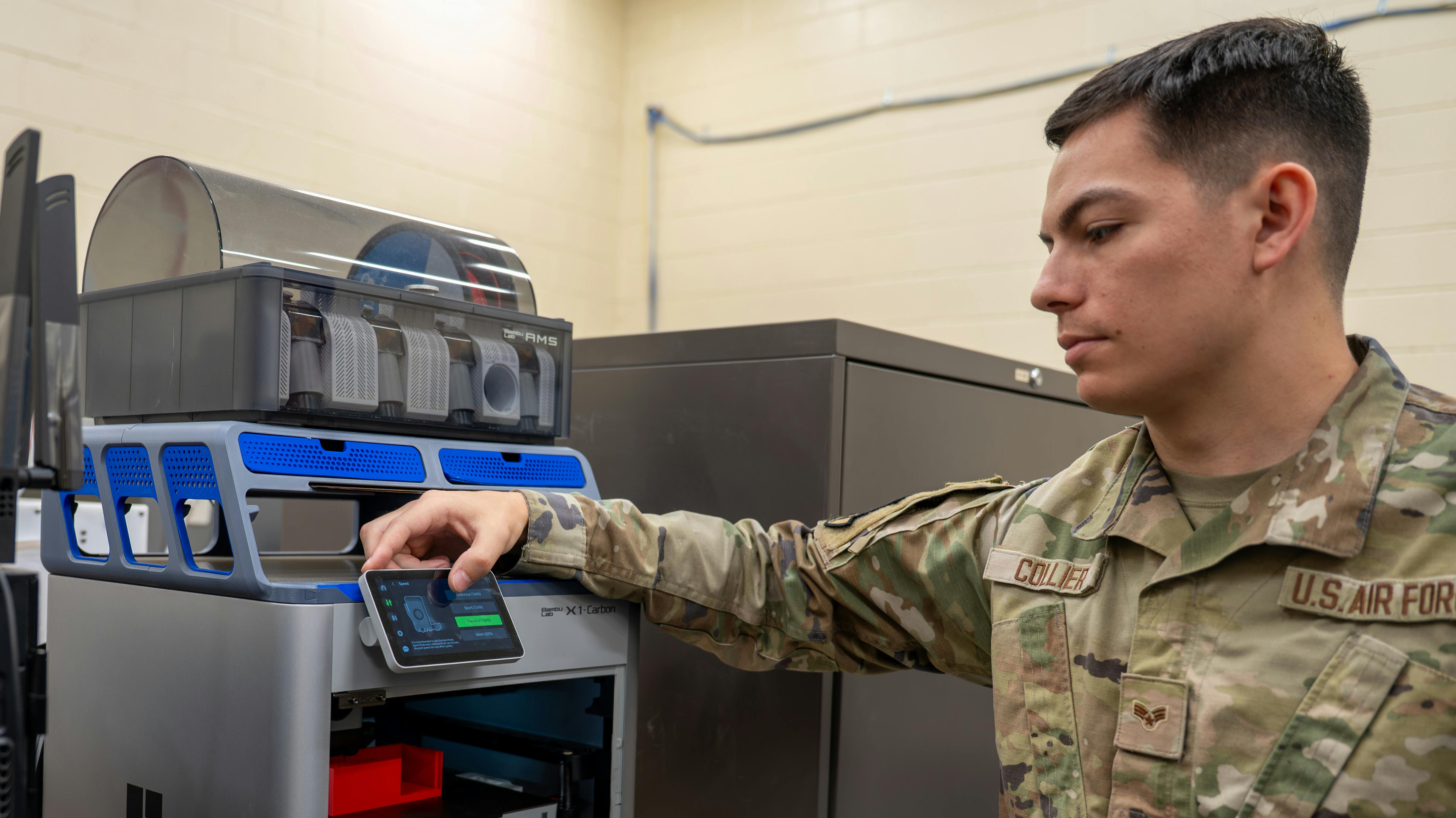 A man wearing military clothing touching the screen of a 3D printer