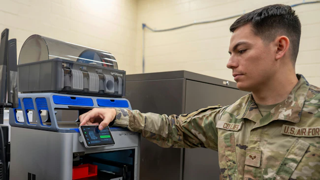 A man wearing military clothing touching the screen of a 3D printer