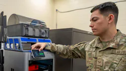 A man wearing military clothing touching the screen of a 3D printer A man wearing military clothing touching the screen of a 3D printer