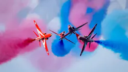 Four red airplanes flying in close formation around each other with pink and blue plumes of smoke in the air Four red airplanes flying in close formation around each other with pink and blue plumes of smoke in the air