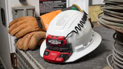 A white hard had with a red attachment on it sitting on a black table with orange gloves sitting behind the helmet A white hard had with a red attachment on it sitting on a black table with orange gloves sitting behind the helmet