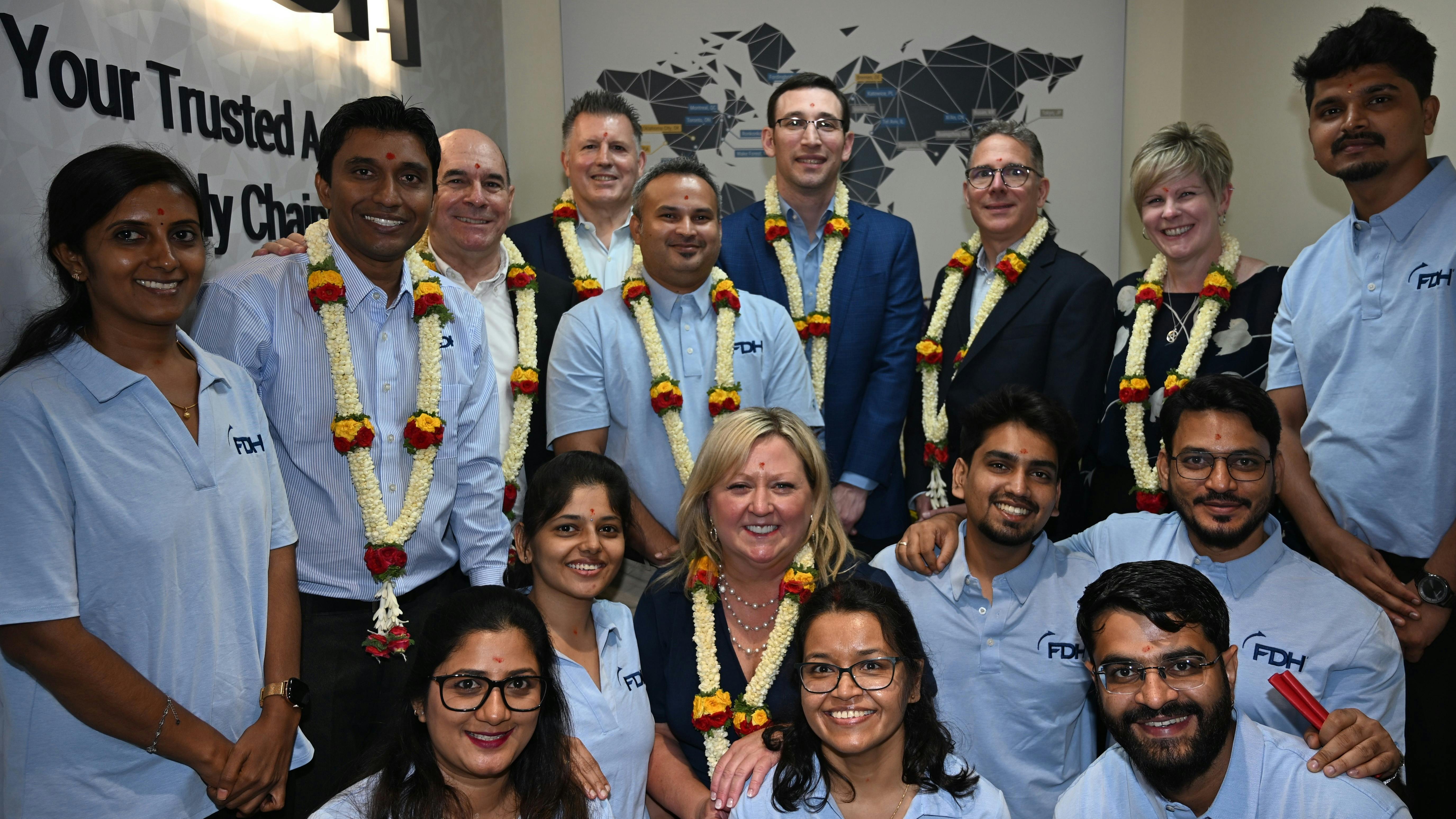 A group of technicians in light blue polo shirts posing with professionals in business attire