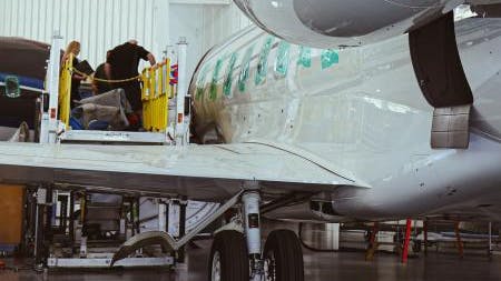 A technician on a lifted platform working next to a parked airplane inside a hangar