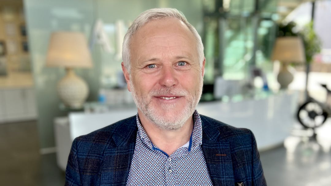 A man wearing a blue shirt and black blazer smiling at the camera