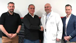 Four men standing in a line and smiling at the camera, with three dressed in business-casual attire and one in a white lab coat Four men standing in a line and smiling at the camera, with three dressed in business-casual attire and one in a white lab coat