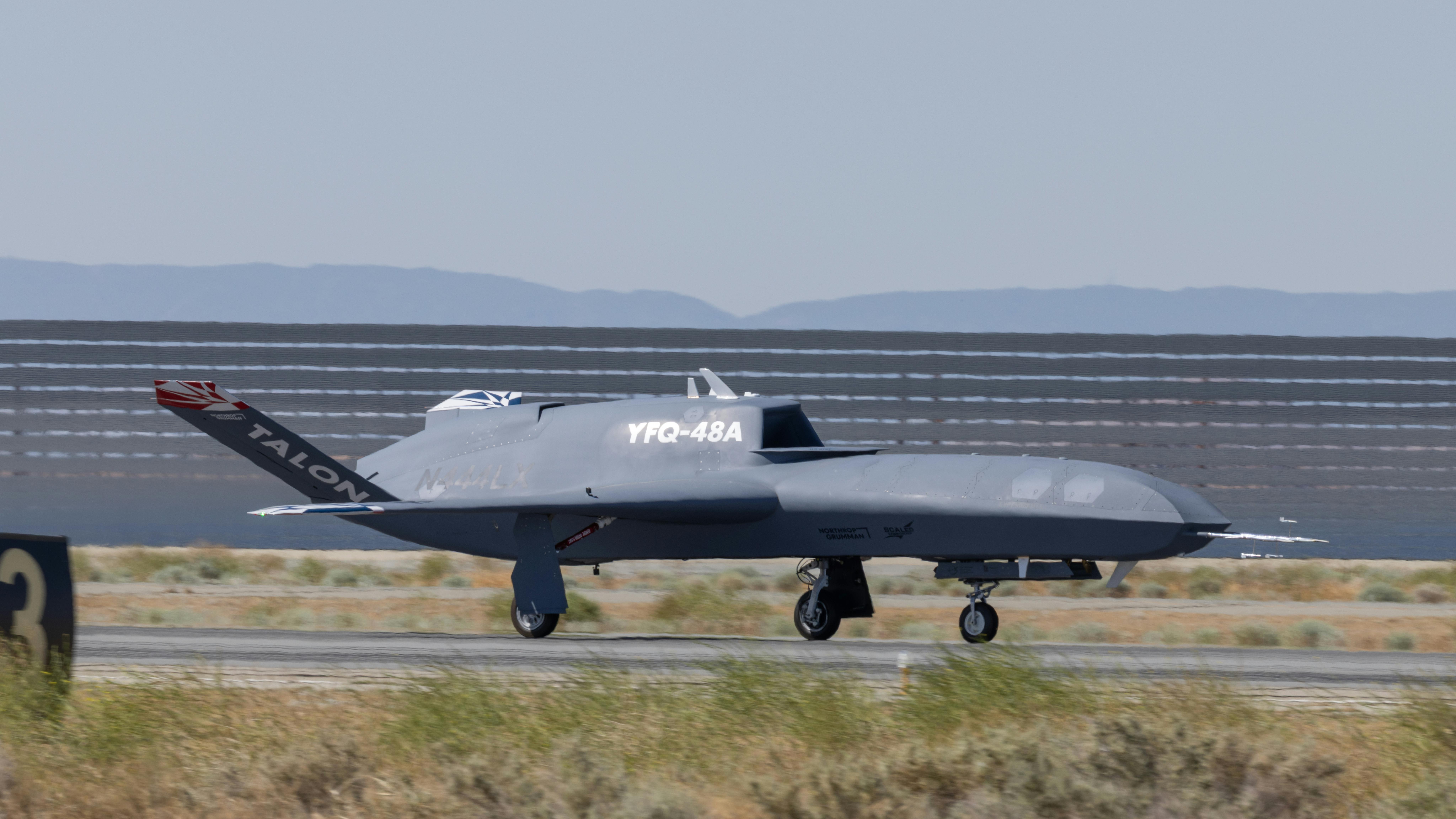 A black military aircraft parked on the ground with white text on the side that reads: YFQ-48A
